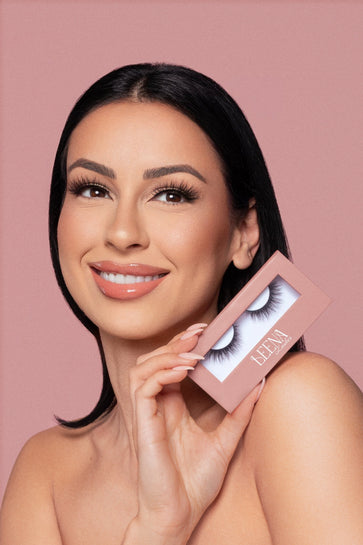 Woman holding a box of wispy natural false eyelashes against a pink background